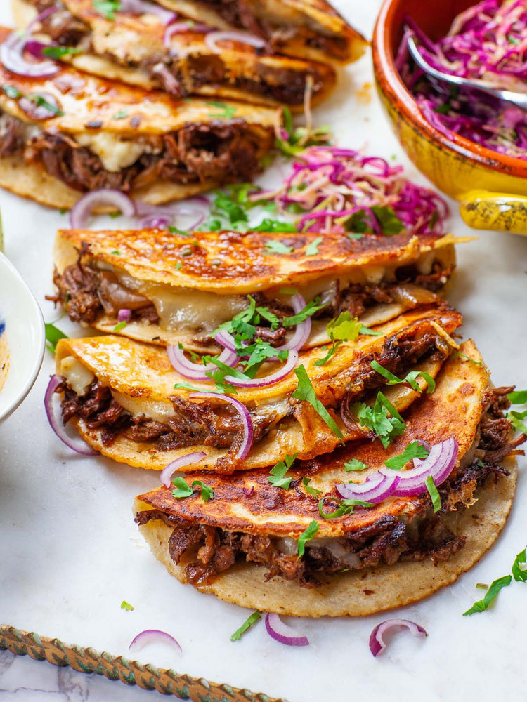 Mouthwatering birria tacos with melted cheese, garnished with onions and cilantro, served with slaw on a platter.