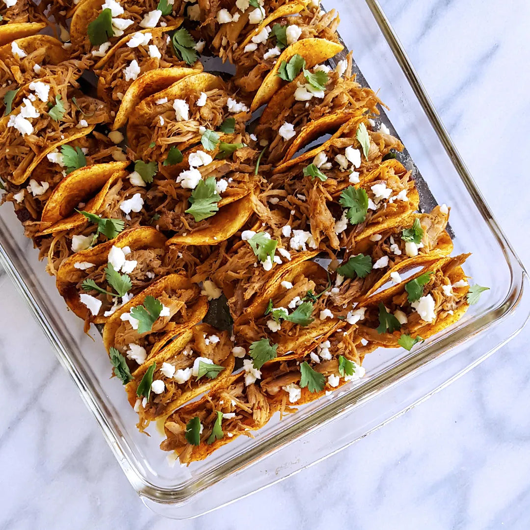 Tray of mini tacos filled with shredded meat, cheese, and cilantro.