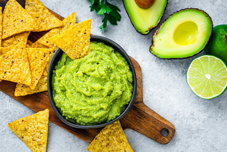 Bowl of guacamole with tortilla chips, avocados, and lime on a wooden board.
