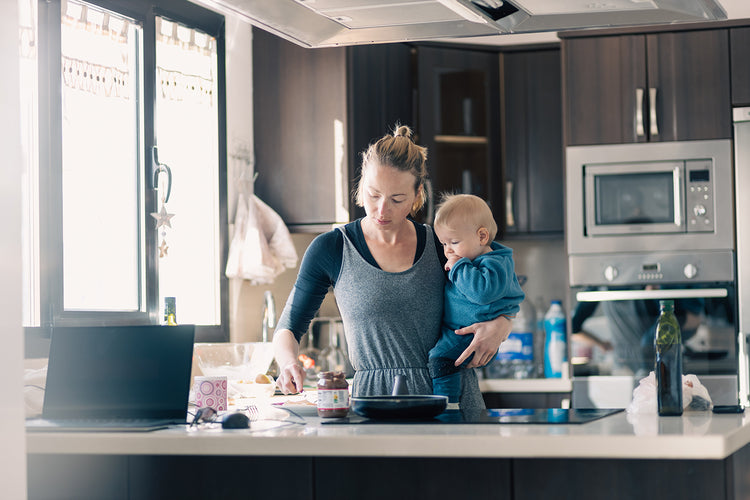 A woman holding a baby while preparing food in a modern kitchen.